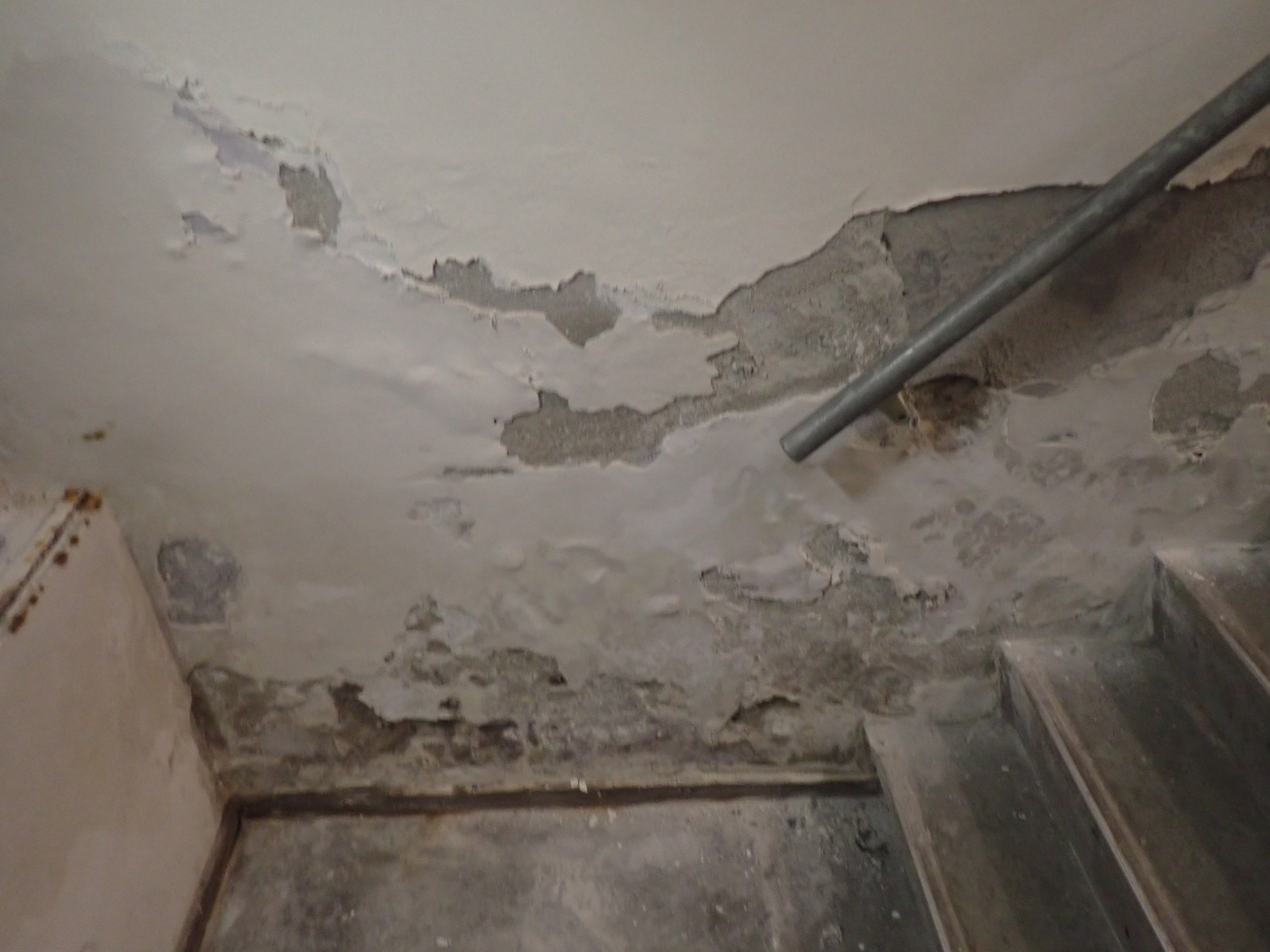 Kelderplafond met vochtschade rond leidingwerk en trap — beeld bij vocht of lekkage in kelder